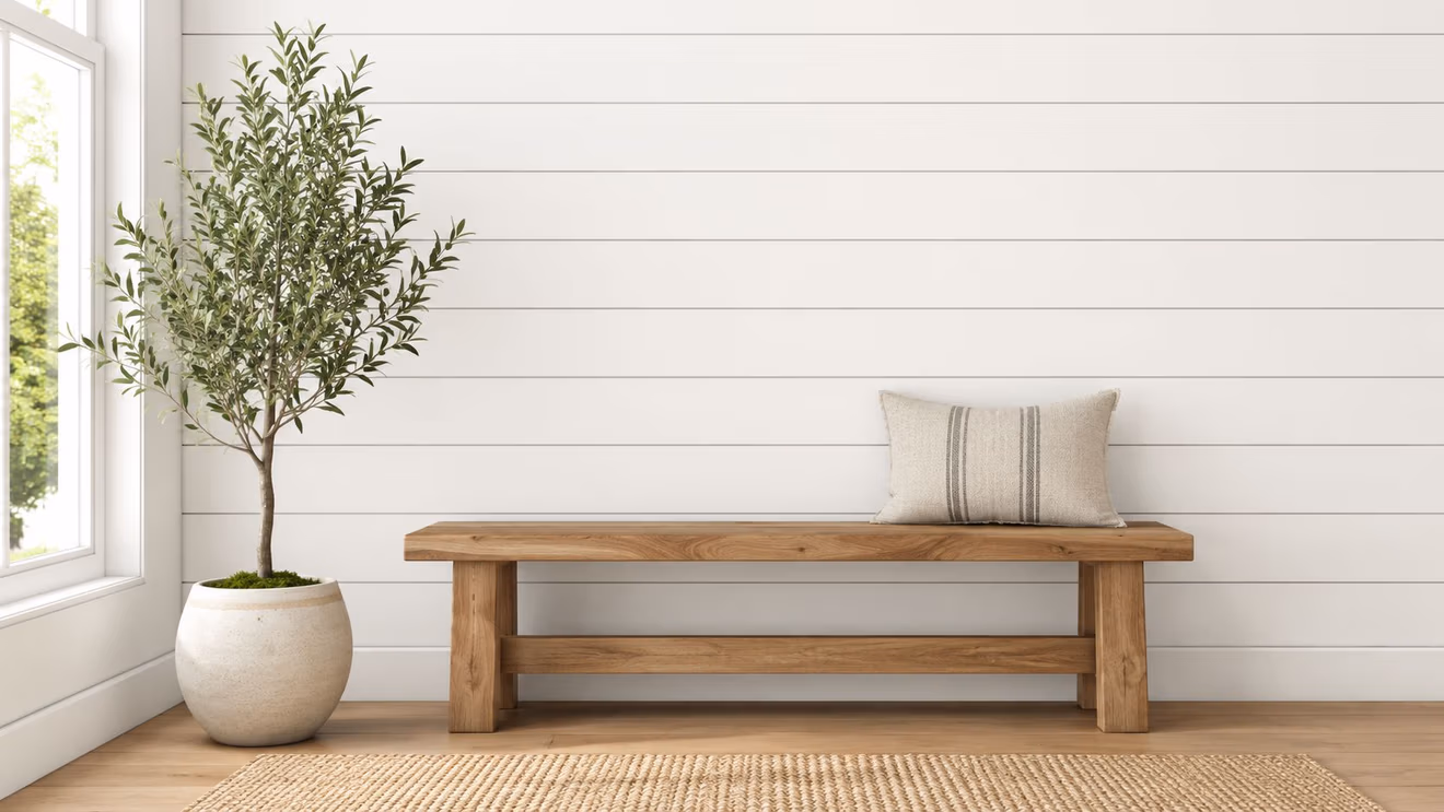 A rustic wooden bench with a striped throw pillow sits next to a potted tree in a bright room.