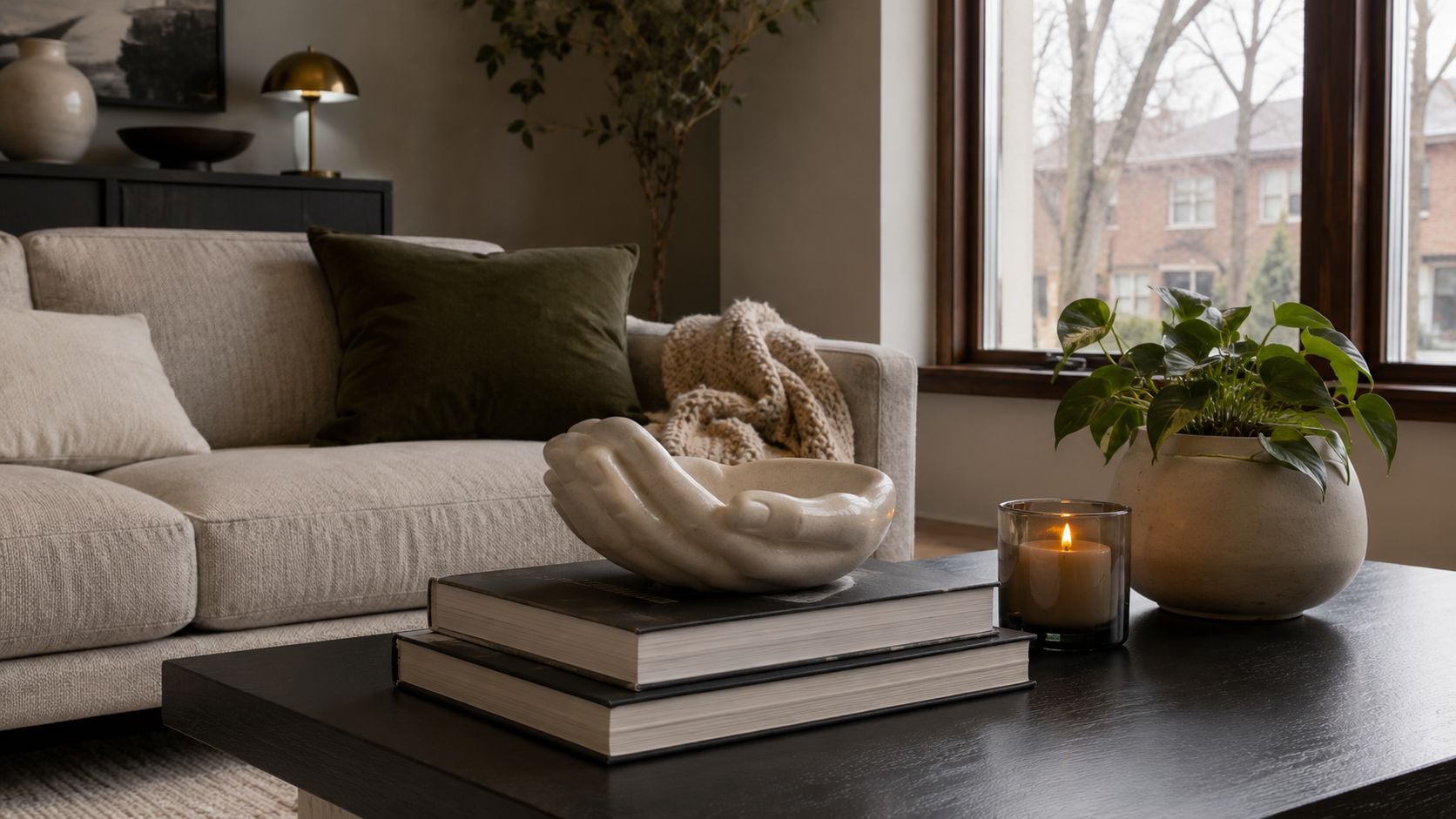 A unique hand-shaped bowl sits atop stacked books on a modern black coffee table in a living room.