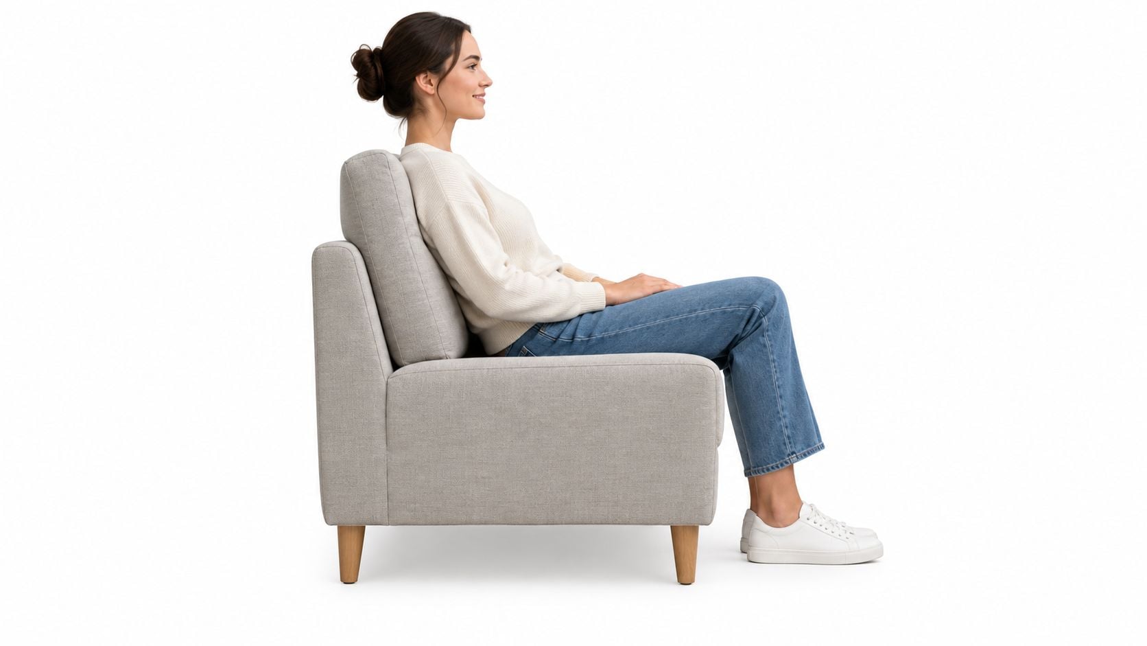 A woman with her hair in a bun sitting on a modern light gray tight back armchair.